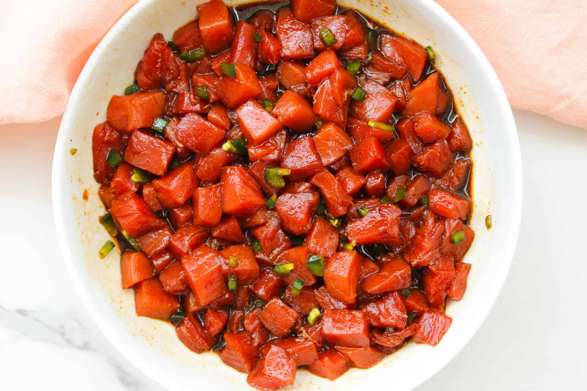 Ahi tuna poke marinating in a white bowl.
