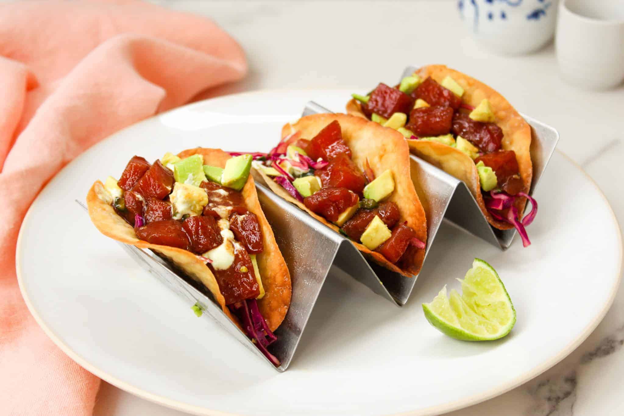 Ahi Tuna Tacos (Poke Tacos) on a white plate with a salmon colored towel and lime wedge.