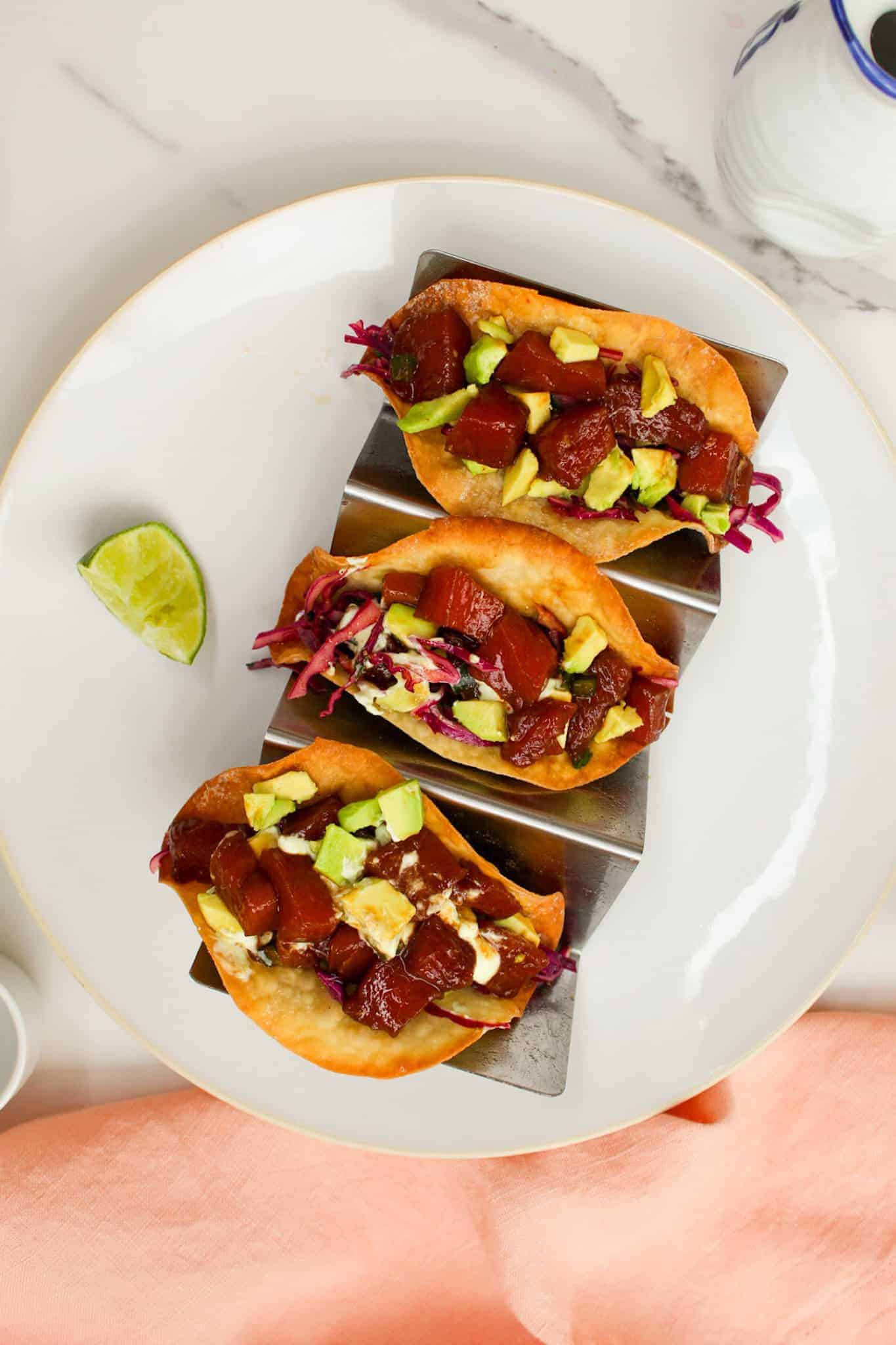 Overheat image of tuna tacos on a white plate with a lime wedge.