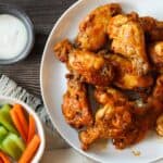 Crockpot chicken wings tossed in buffalo sauce on a white plate.