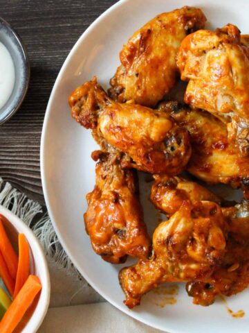 Crockpot chicken wings tossed in buffalo sauce on a white plate.
