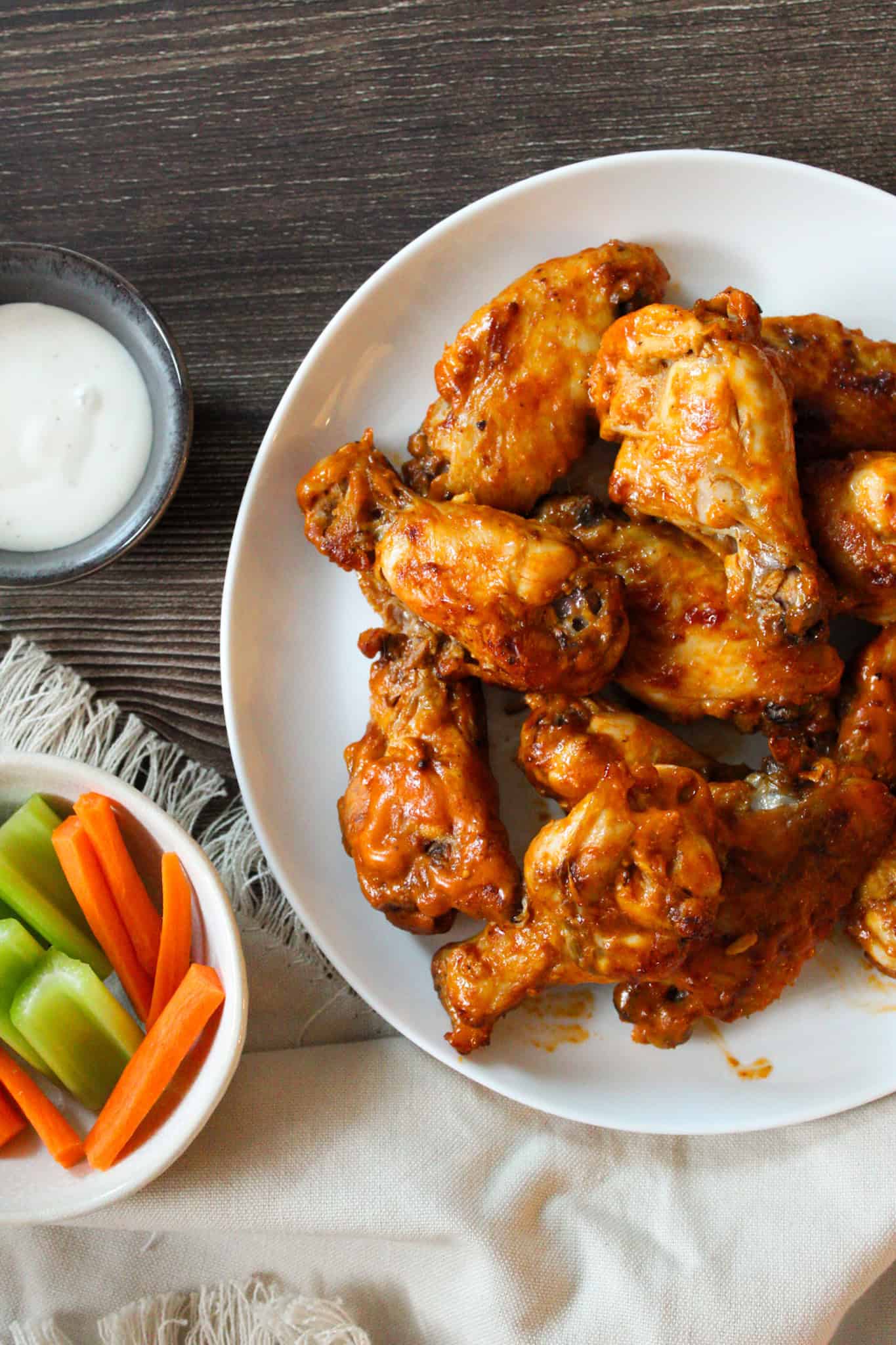 Crockpot Chicken Wings stacked on a white plate next to a cup of ranch and veggies.
