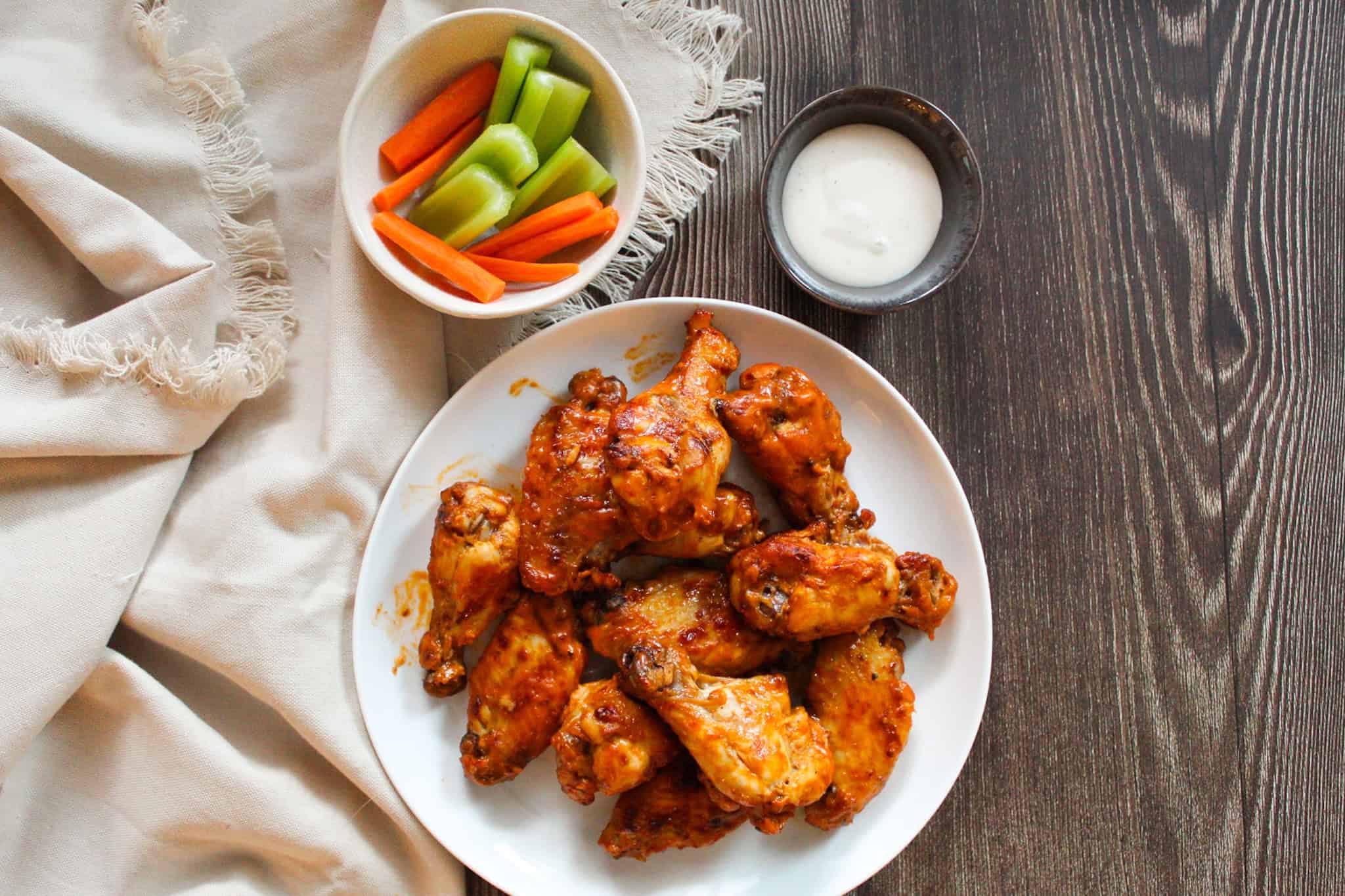 Wings on a plate next to ranch and veggies on a wood surface.
