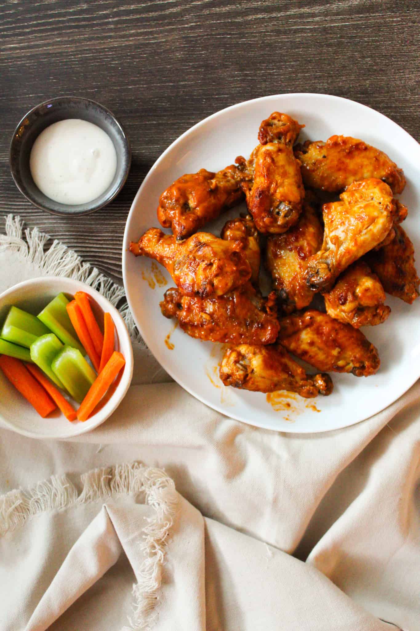 Hot wings on a white plate next to ranch, celery, and carrots.
