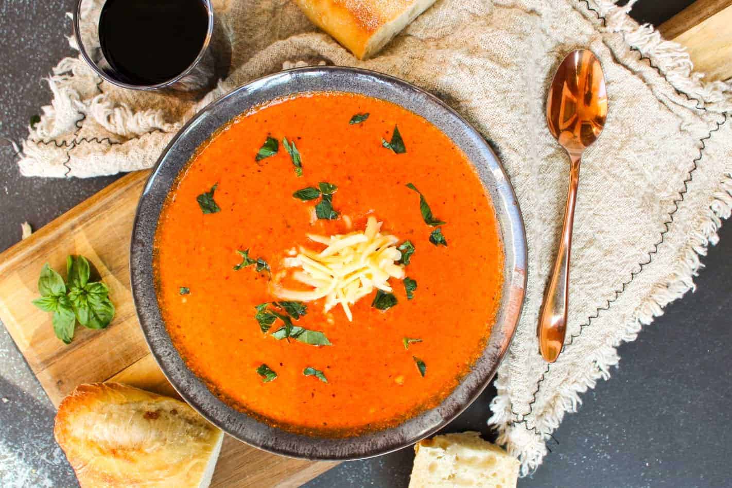 Creamy Roasted Red Pepper Soup with Gouda in a grey bowl sitting on a cutting board.