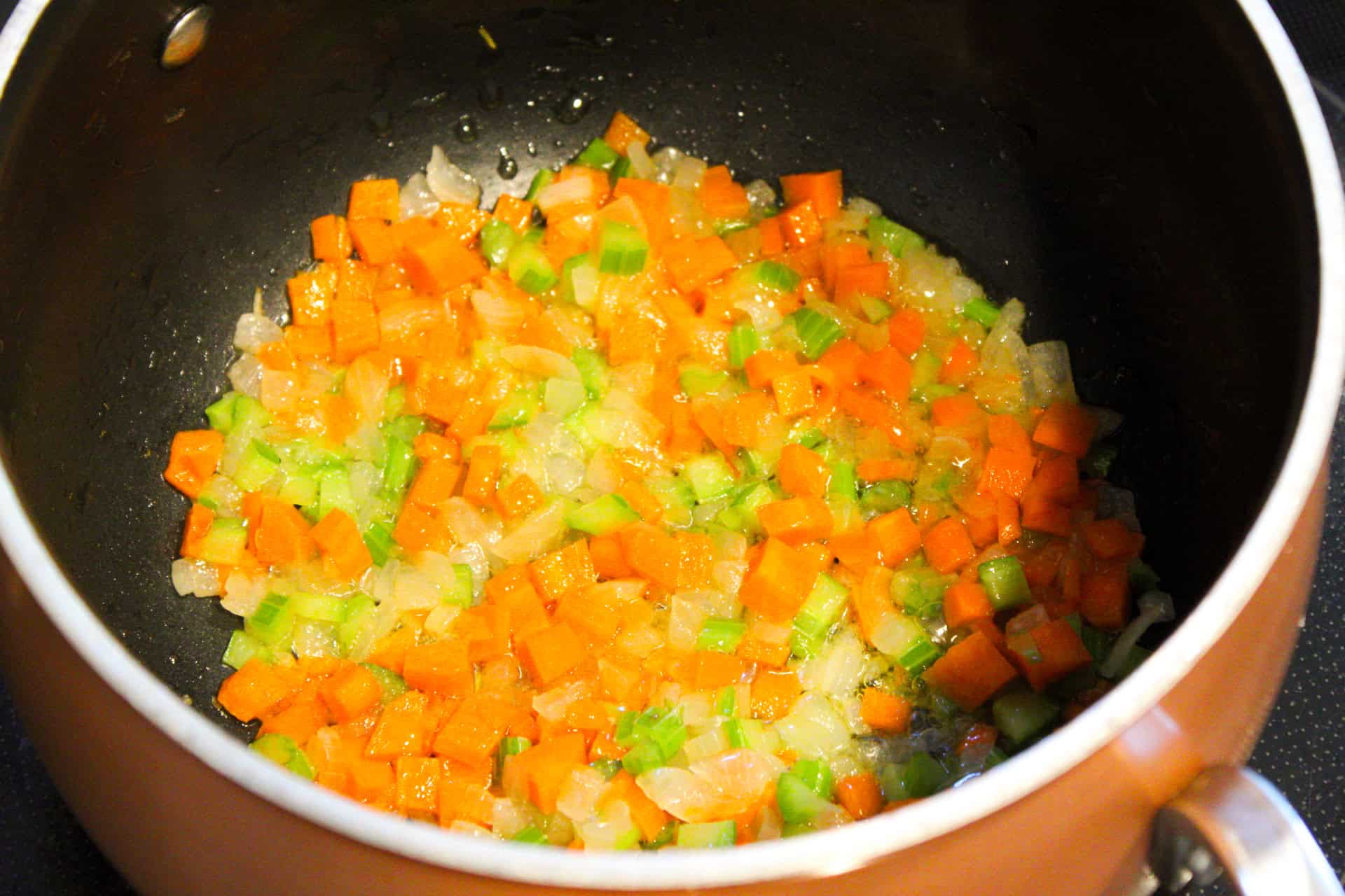 Sauteing onions, carrots, celery, and garlic in a copper pot. 