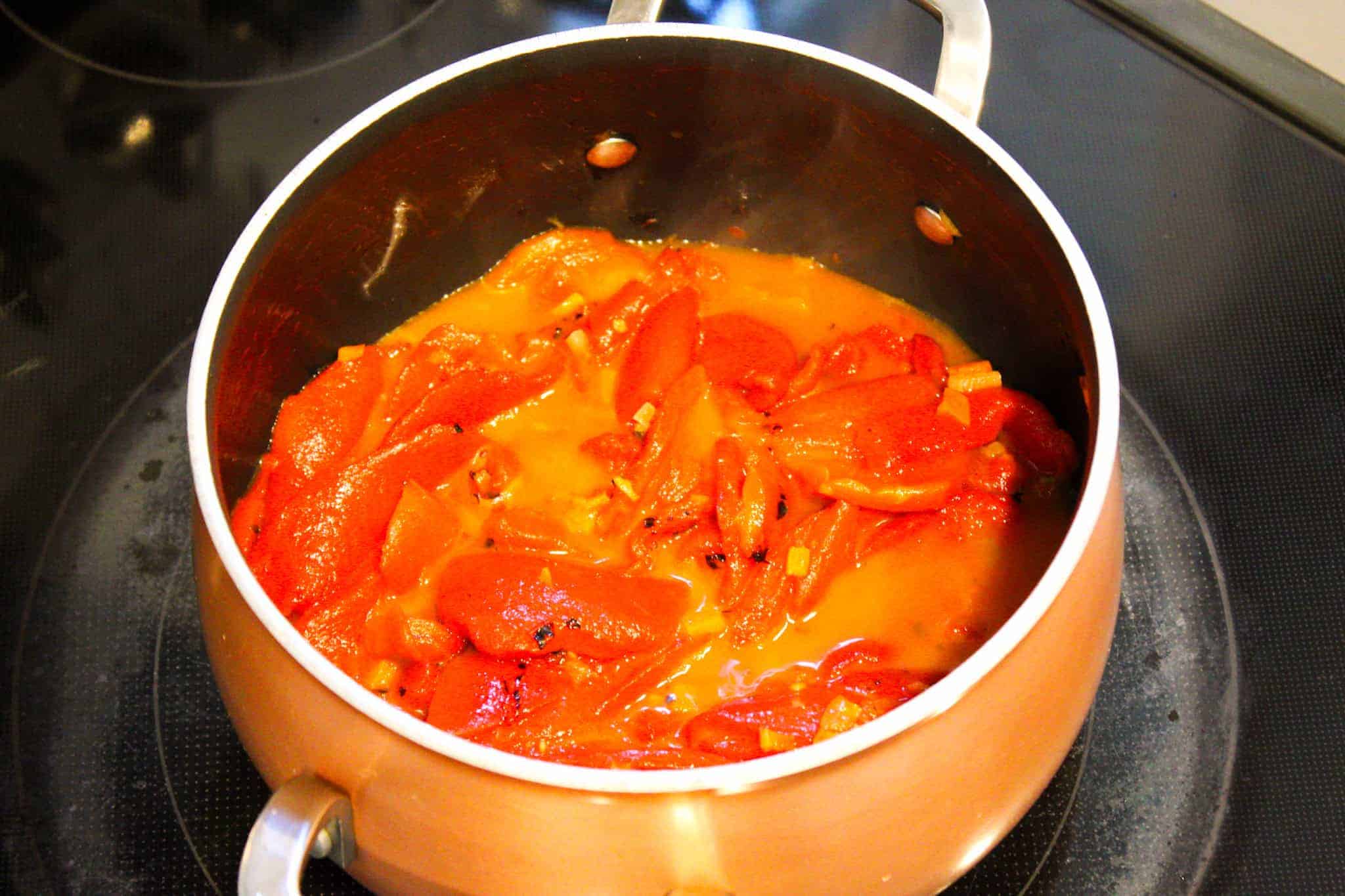 Roasted red peppers simmering in broth in a copper pot.