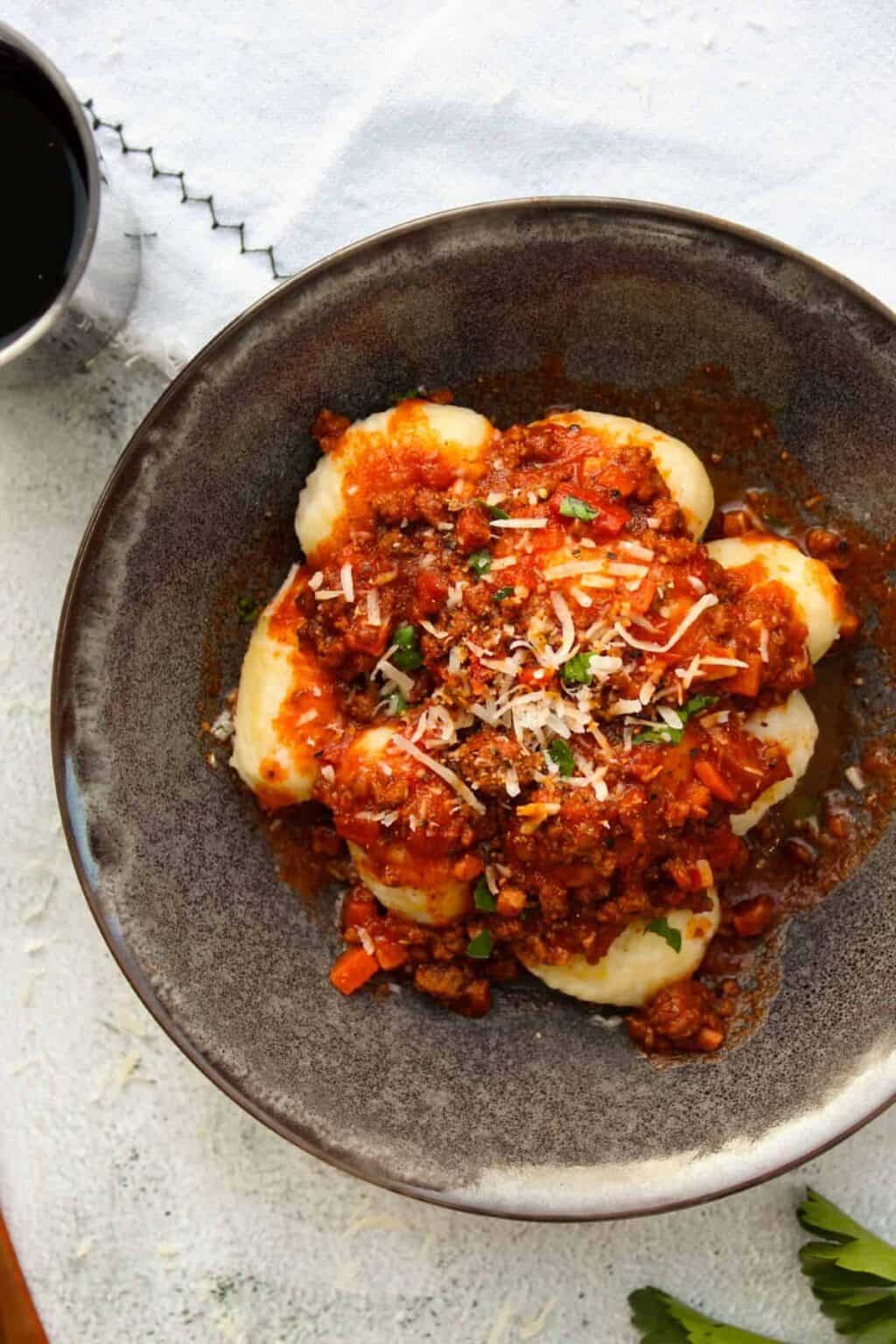 Homemade gnocchi bolognese in a charcoal bowl on a white towel.