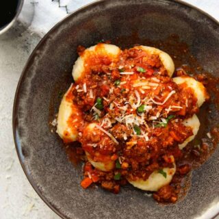 Homemade gnocchi bolognese in a charcoal bowl on a white towel.