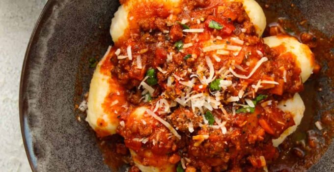 Homemade gnocchi bolognese in a charcoal bowl on a white towel.