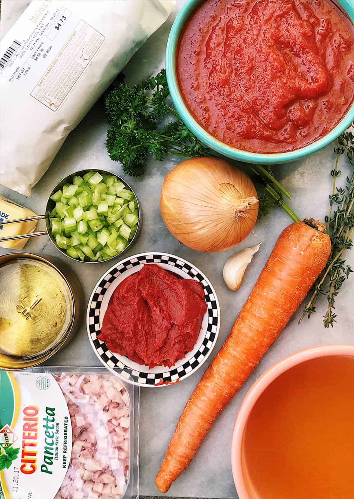 Bolognese sauce ingredients on marble counter.