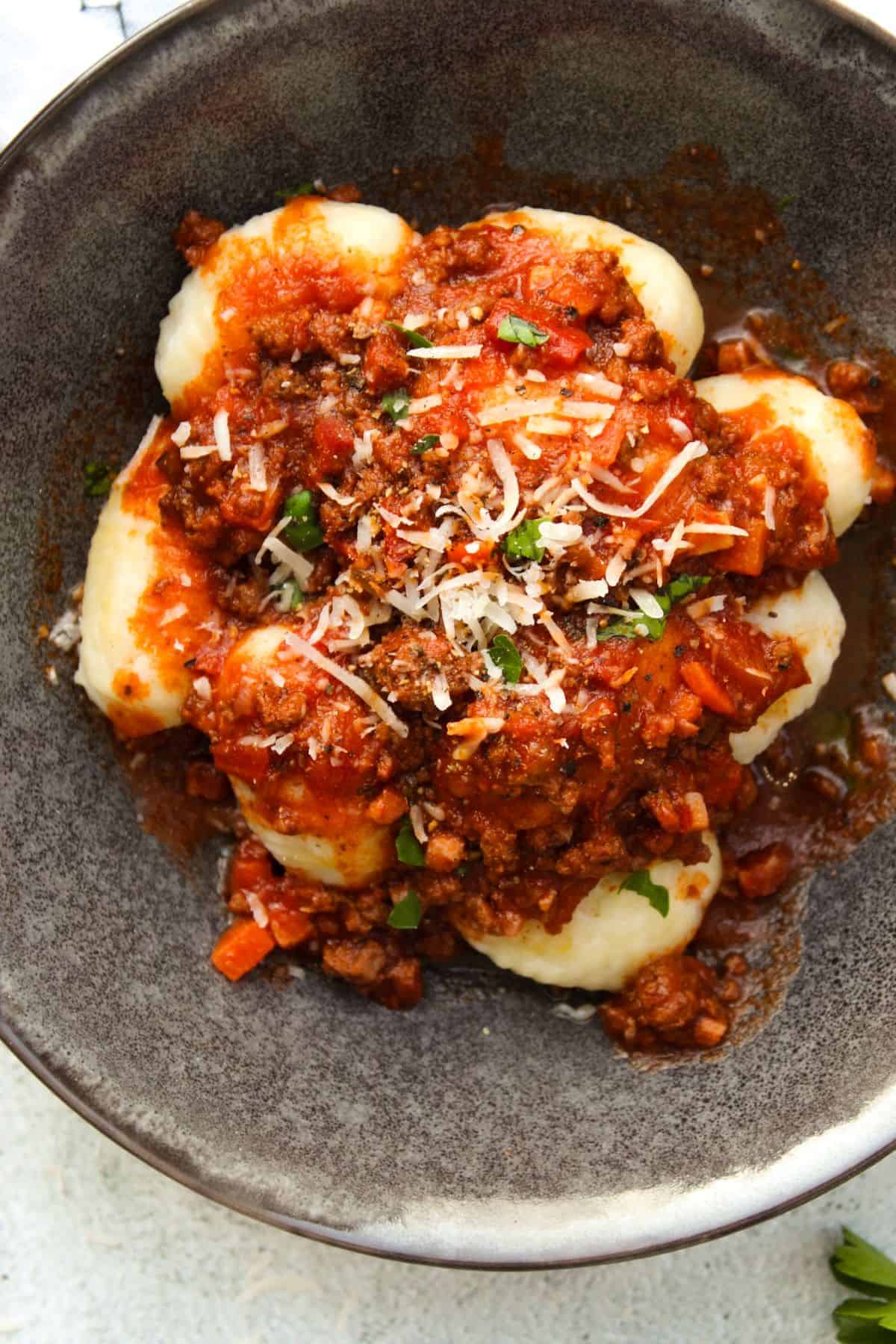 Close up of gnocchi bolognese in a bowl sprinkled with Parmesan and parsley.