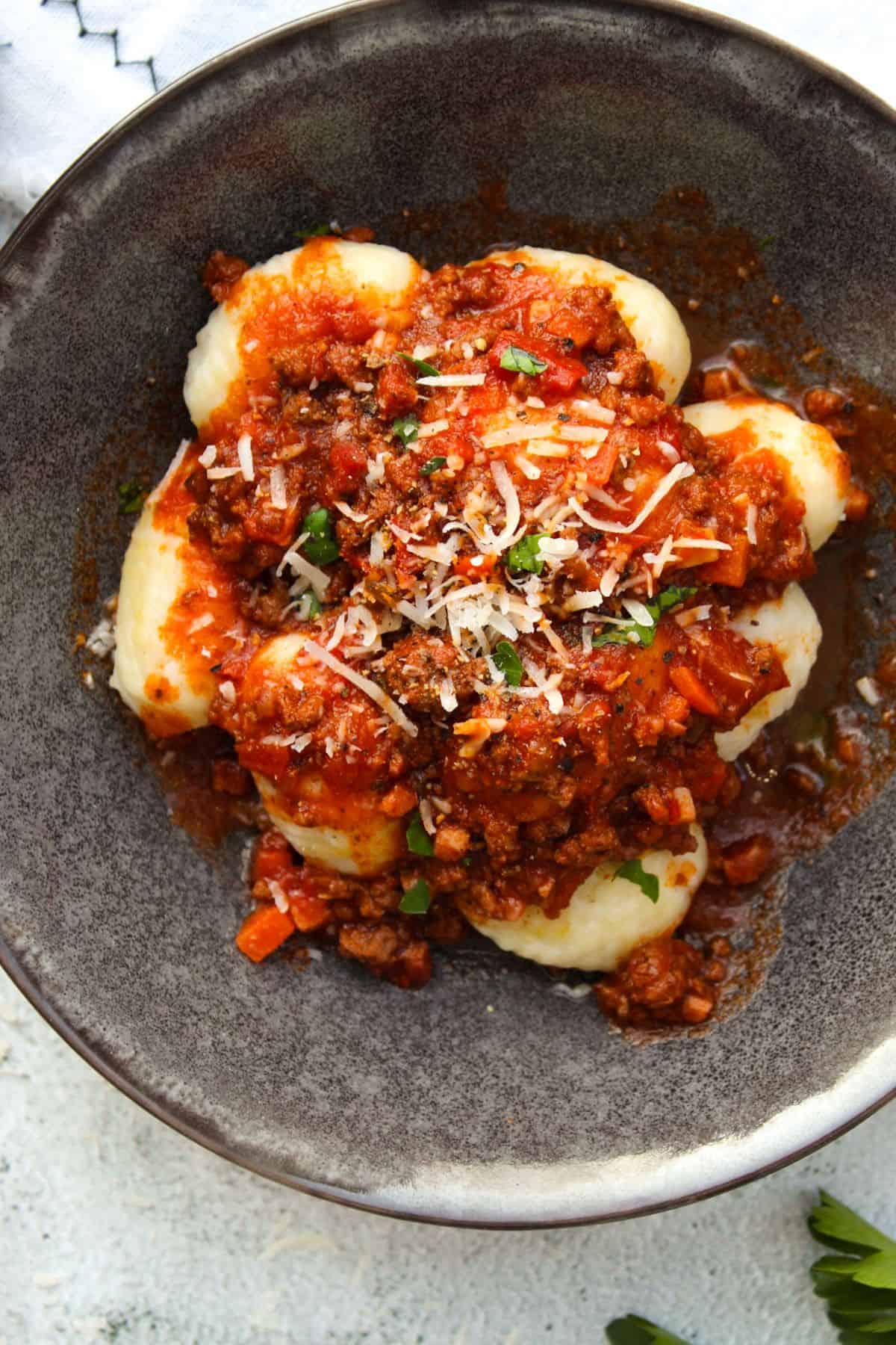 Homemade gnocchi covered in red bolognese sauce, Parmesan, and parsley.