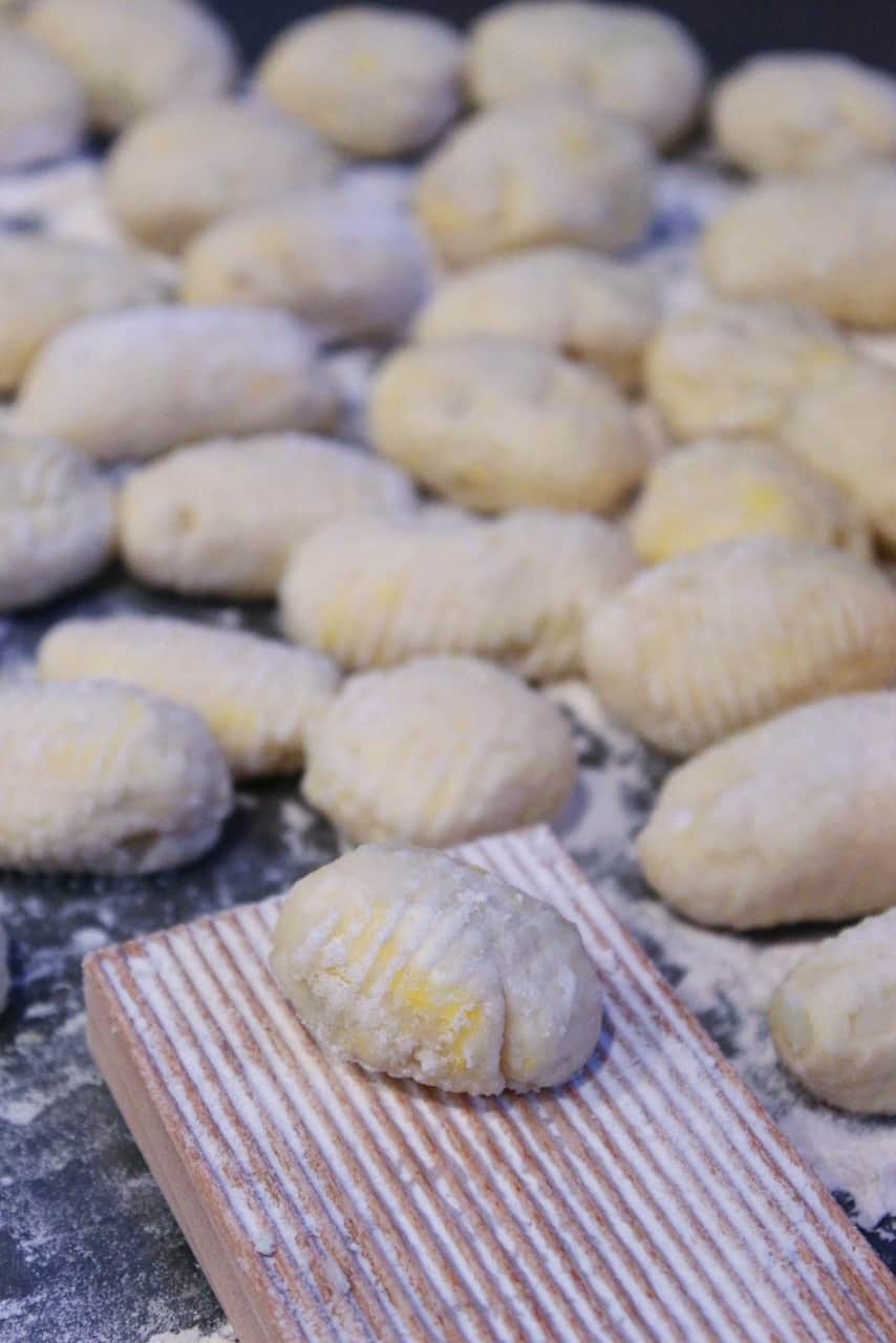Homemade gnocchi being rolled with flour on gnocchi board.
