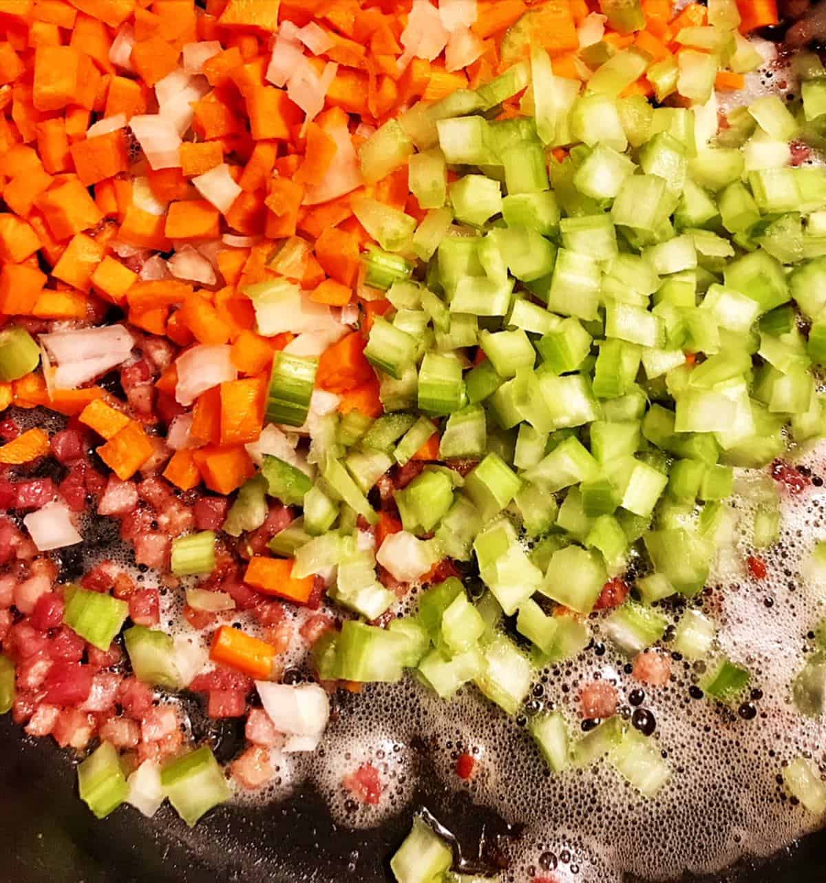 Soffritto of carrots, celery, and onions sauteing with pancetta in a pot.