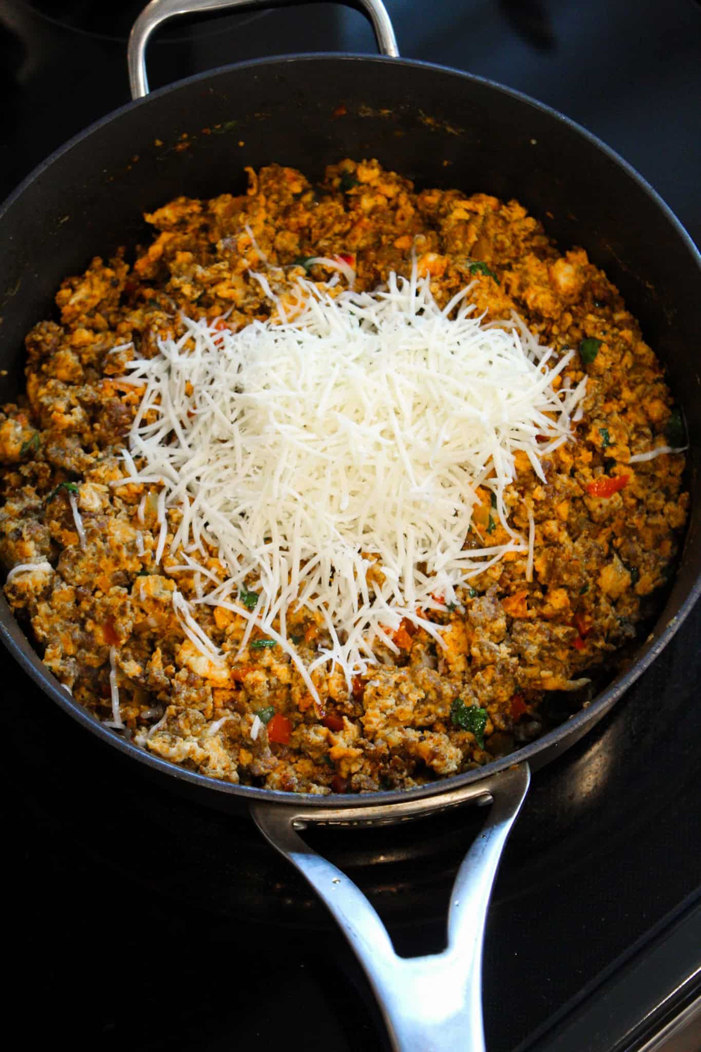 Adding shredded cheese to egg and chorizo mixture in skillet.