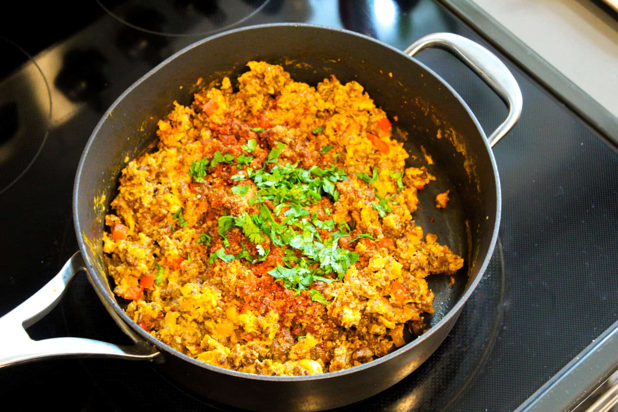 Adding spices and cilantro to skillet with chorizo and egg. 