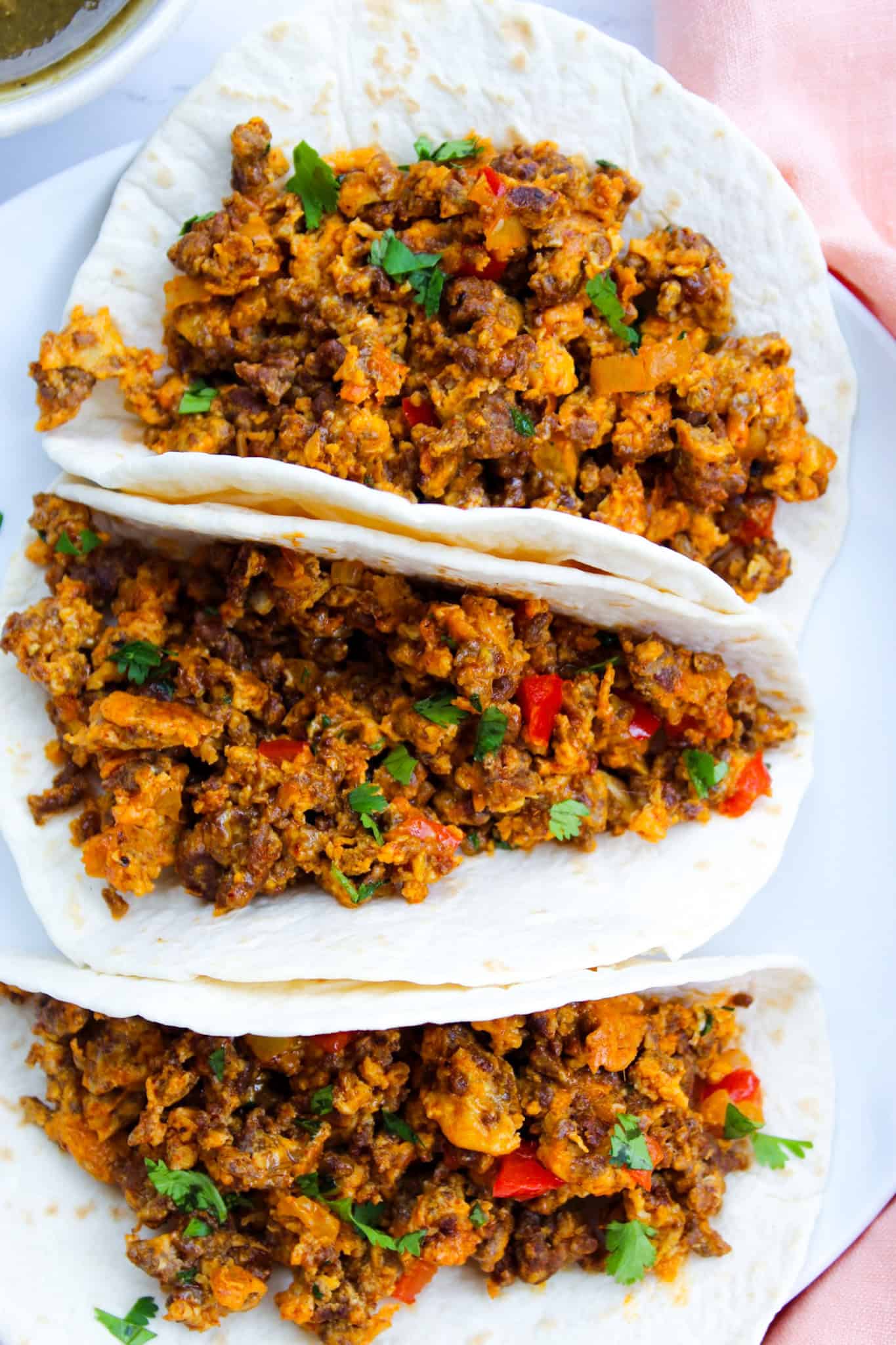 Three breakfast tacos with chorizo and egg on a white plate.
