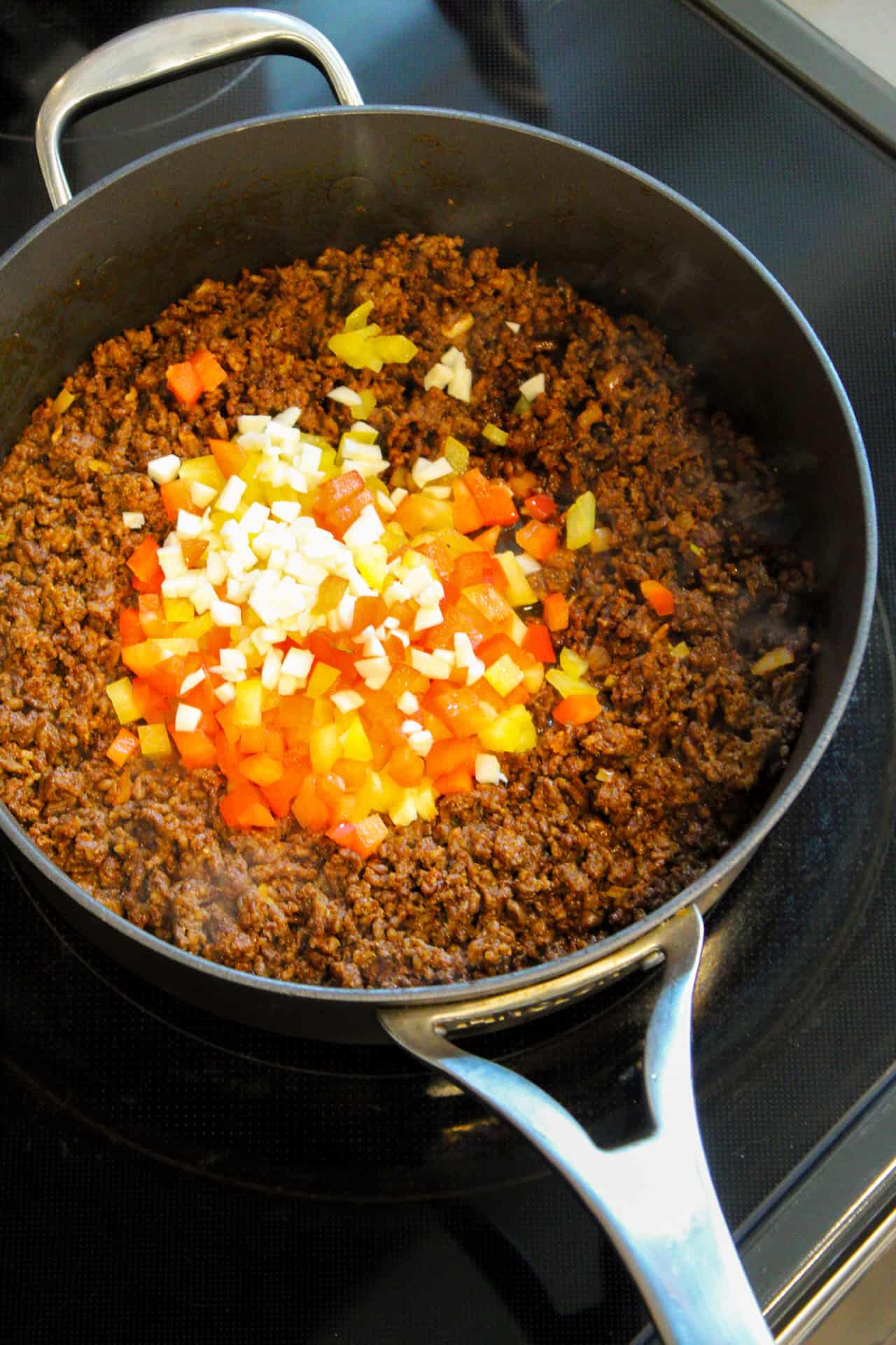 Peppers, onions, and garlic being sauteed in a skillet with chorizo. 