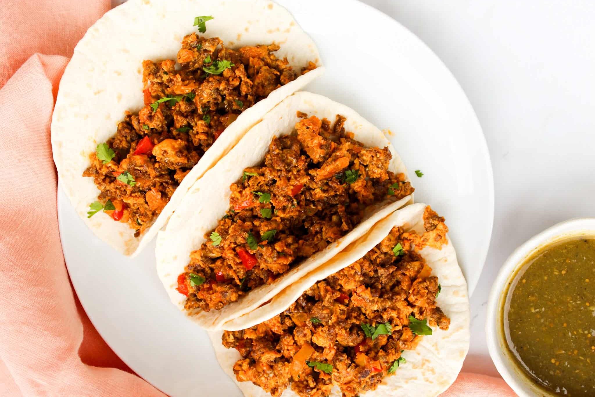 Overhead image of Chorizo Breakfast tacos in tortillas on a white plate. 