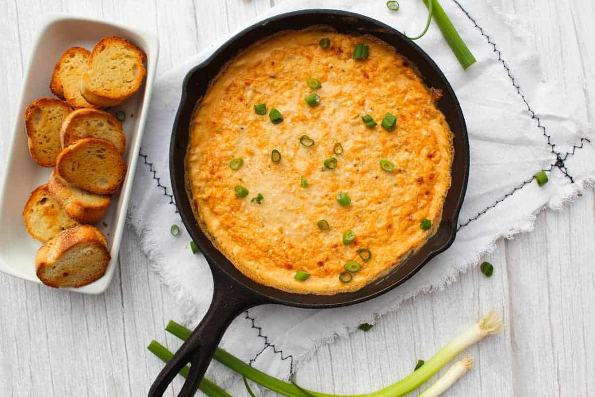 Cajun Crab Dip sprinkled with green onion next to tray of crostini.