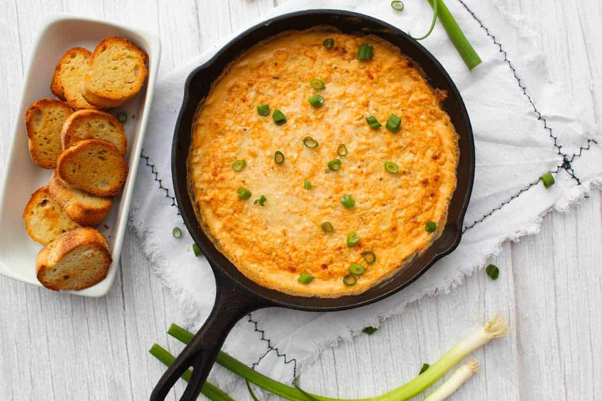Cajun Crab Dip sprinkled with green onion next to tray of crostini.
