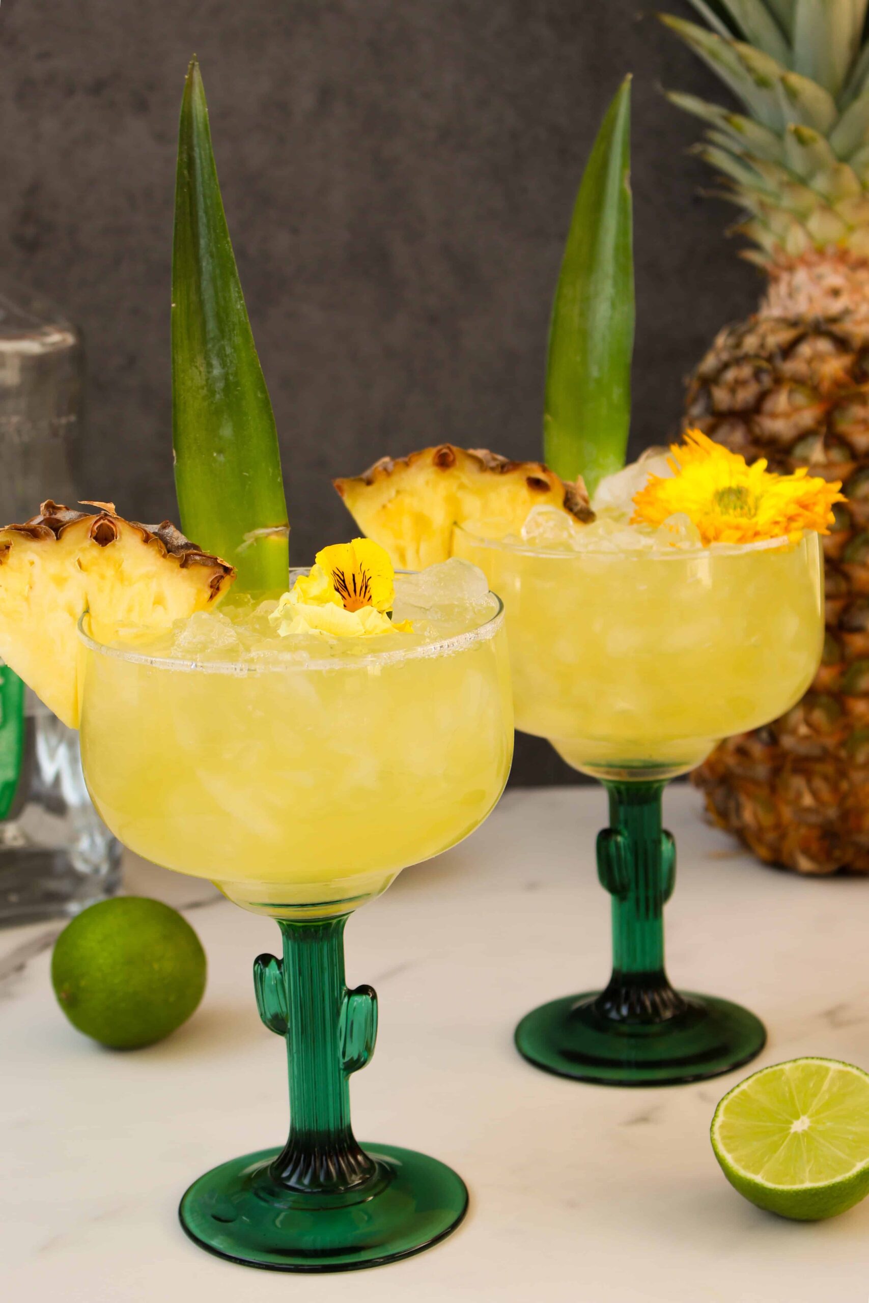 Two cactus shaped glasses with yellow pineapple margarita inside. 