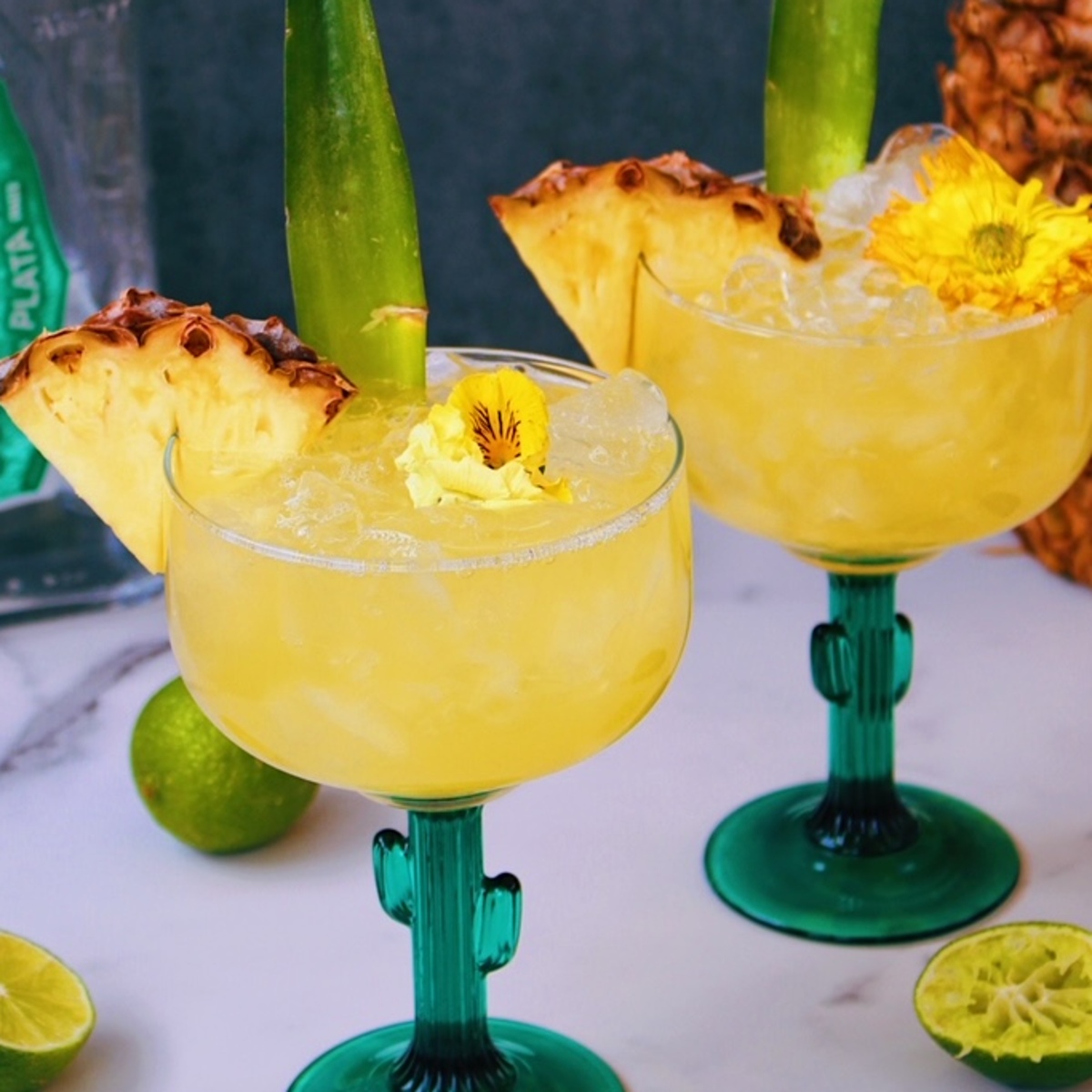 Two Pineapple Tequila Cocktails in cactus shaped glasses garnished with pineapple.