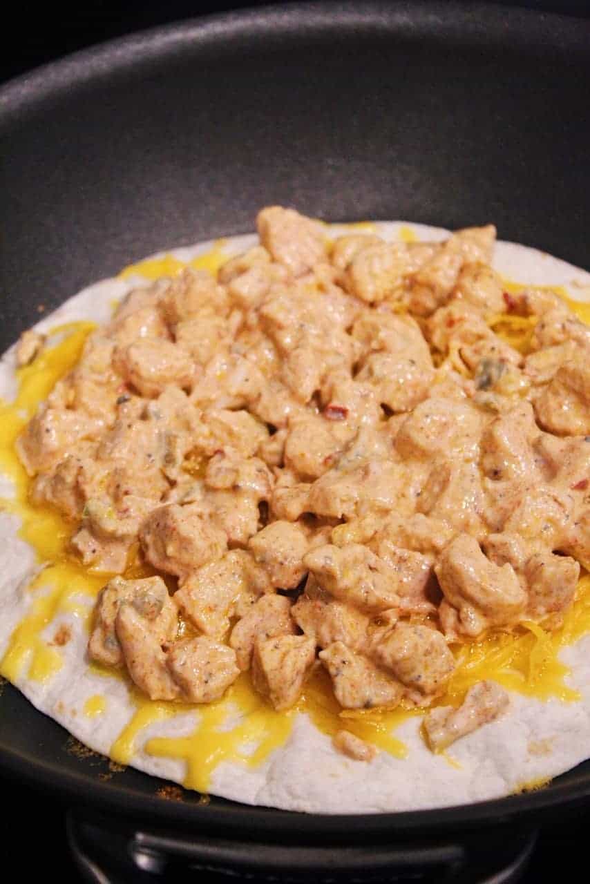 Tortilla topped with cheddar cheese, chicken, and quesadilla sauce.