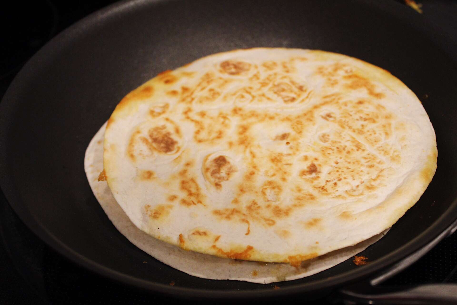 Chicken quesadilla cooking in skillet on stove top.
