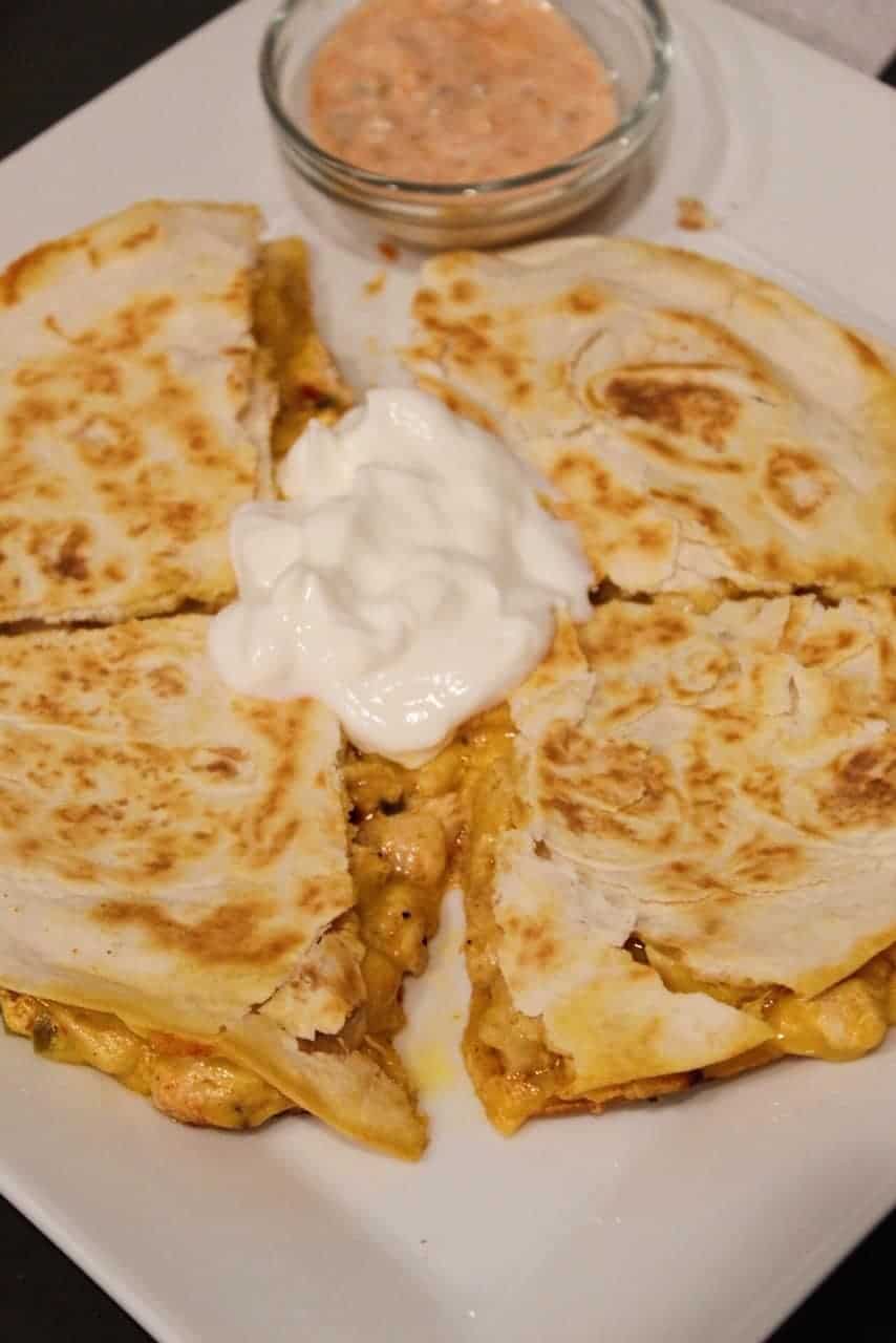 Overhead shot of copycat Taco Bell Chicken Quesadillas topped with sour cream with a side of quesadilla sauce.