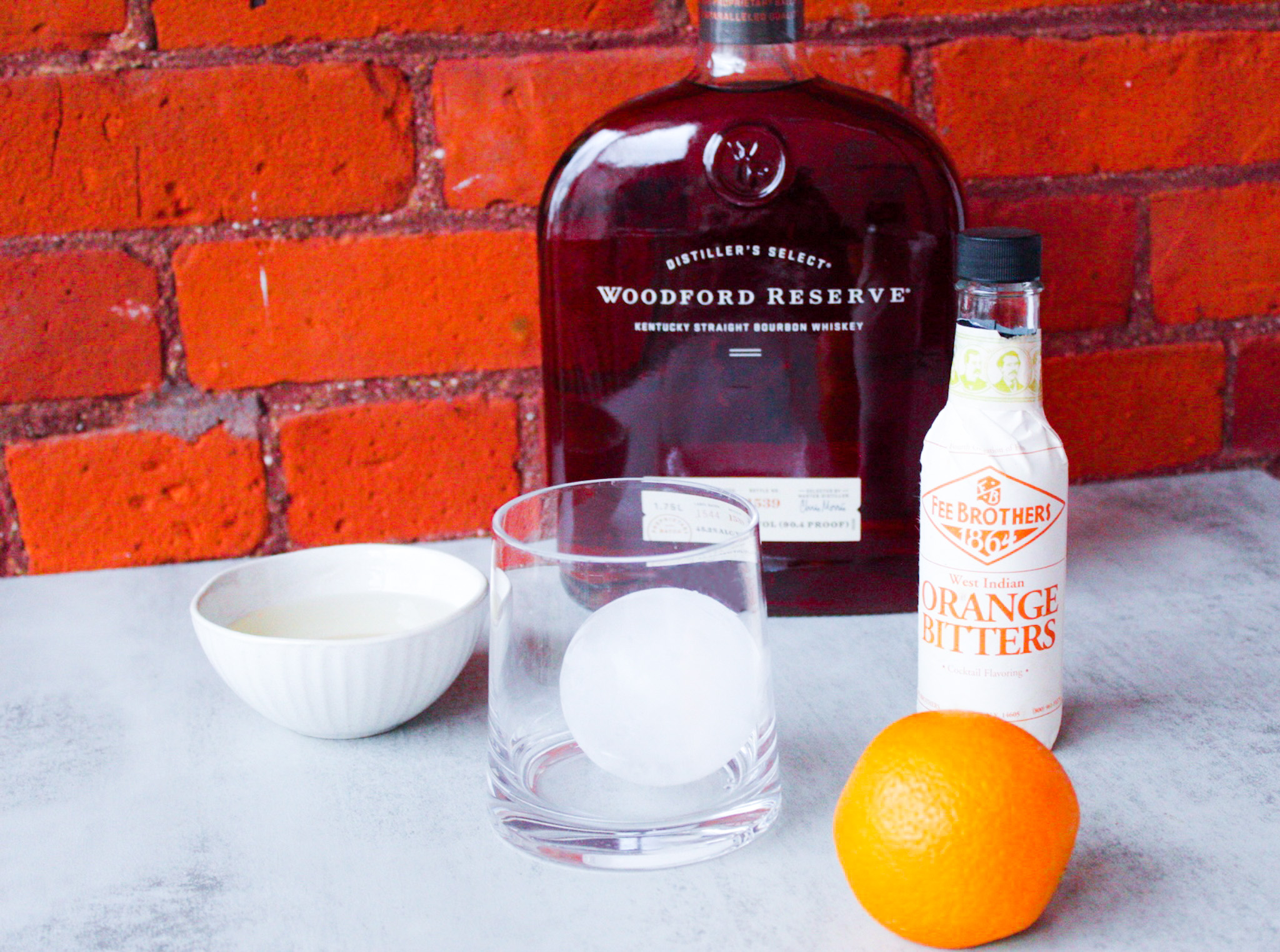 Ingredients for an Old Fashioned sitting in front of brick wall.