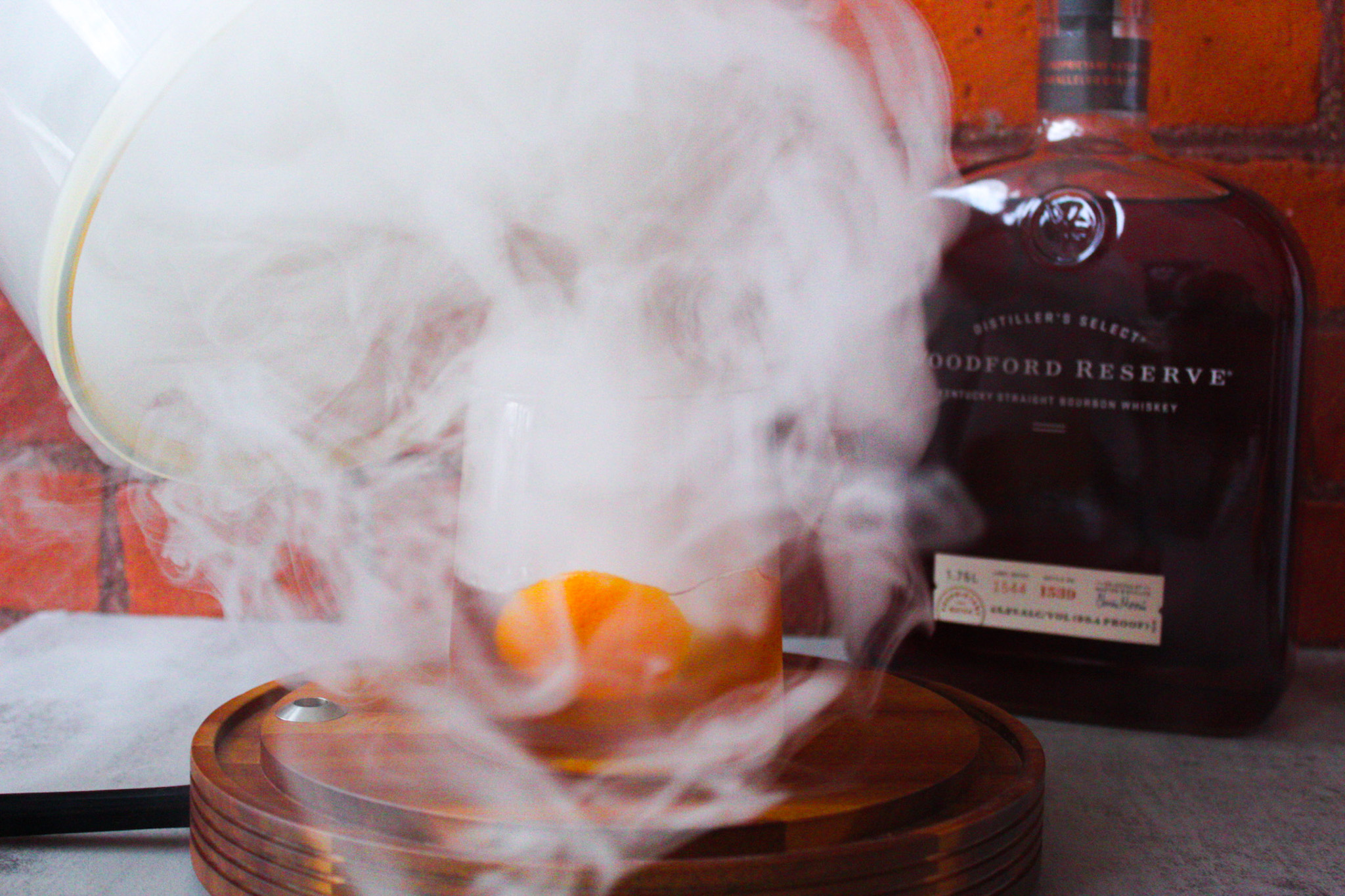 Removing glass cloche from cocktail smoker as smoke swirls around drink.