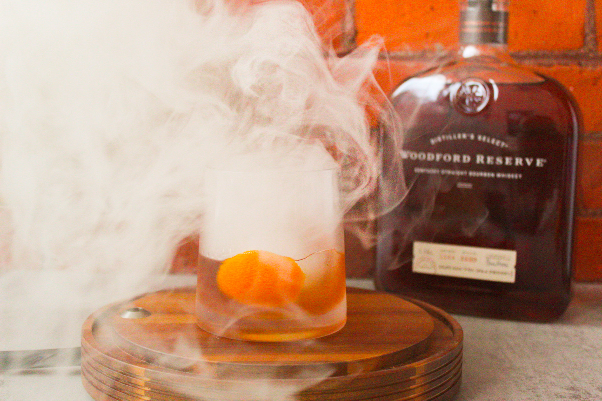 Old Fashioned cocktail sitting on wood base surrounded by smoke.