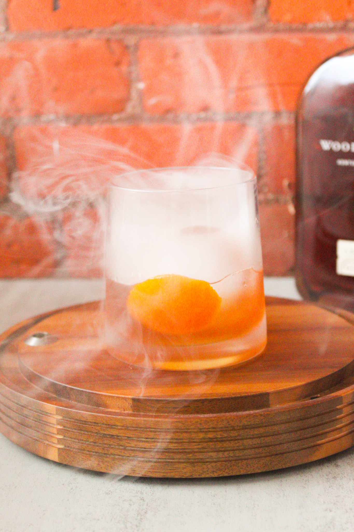 Cocktail sitting on wood base surrounded by smoke. 