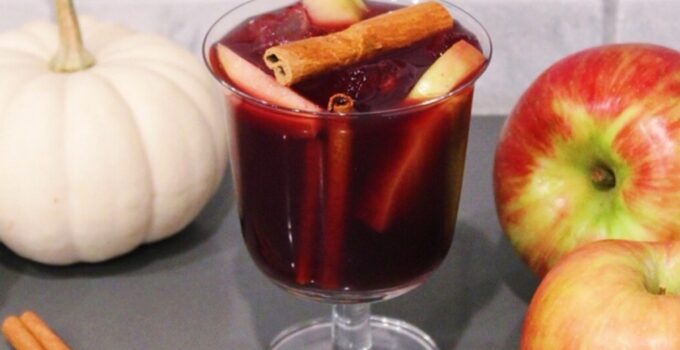 Thanksgiving Sangria in a glass with cinnamon sticks, apples, and pumpkins.