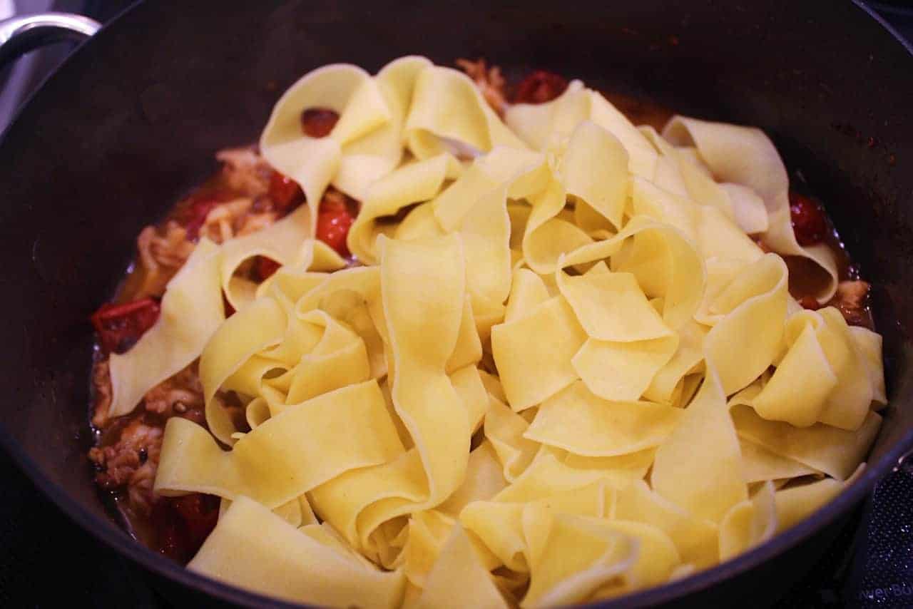 Adding cooked pappardelle noodles to sauce.