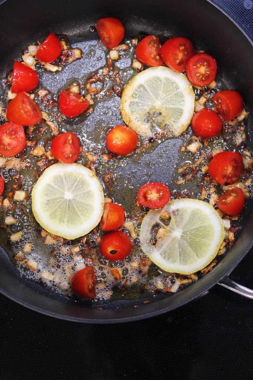 Cooking lemons and grape tomatoes in a pan.