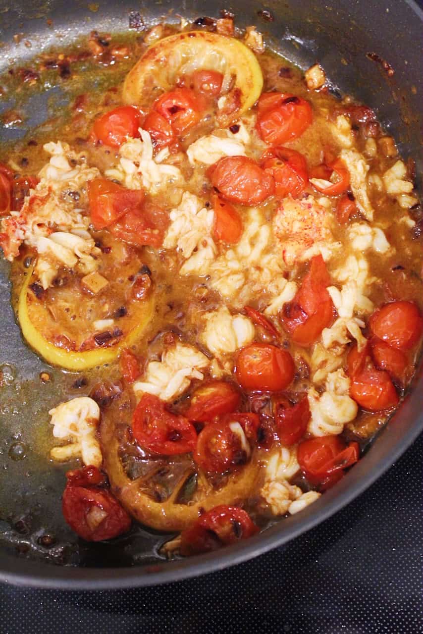Lobster, lemon slices, and tomatoes cooking in white wine sauce.