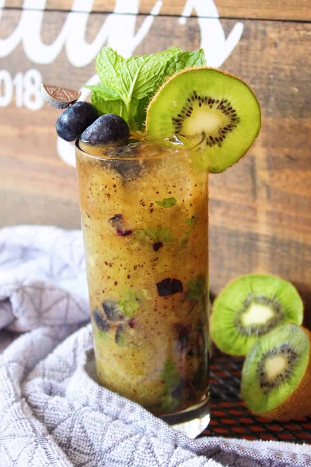 Blueberry Mojito in a tall glass garnished with blueberries, kiwi, and mint.