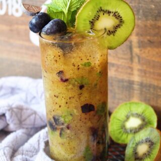 Blueberry Mojito in a tall glass garnished with blueberries, kiwi, and mint.