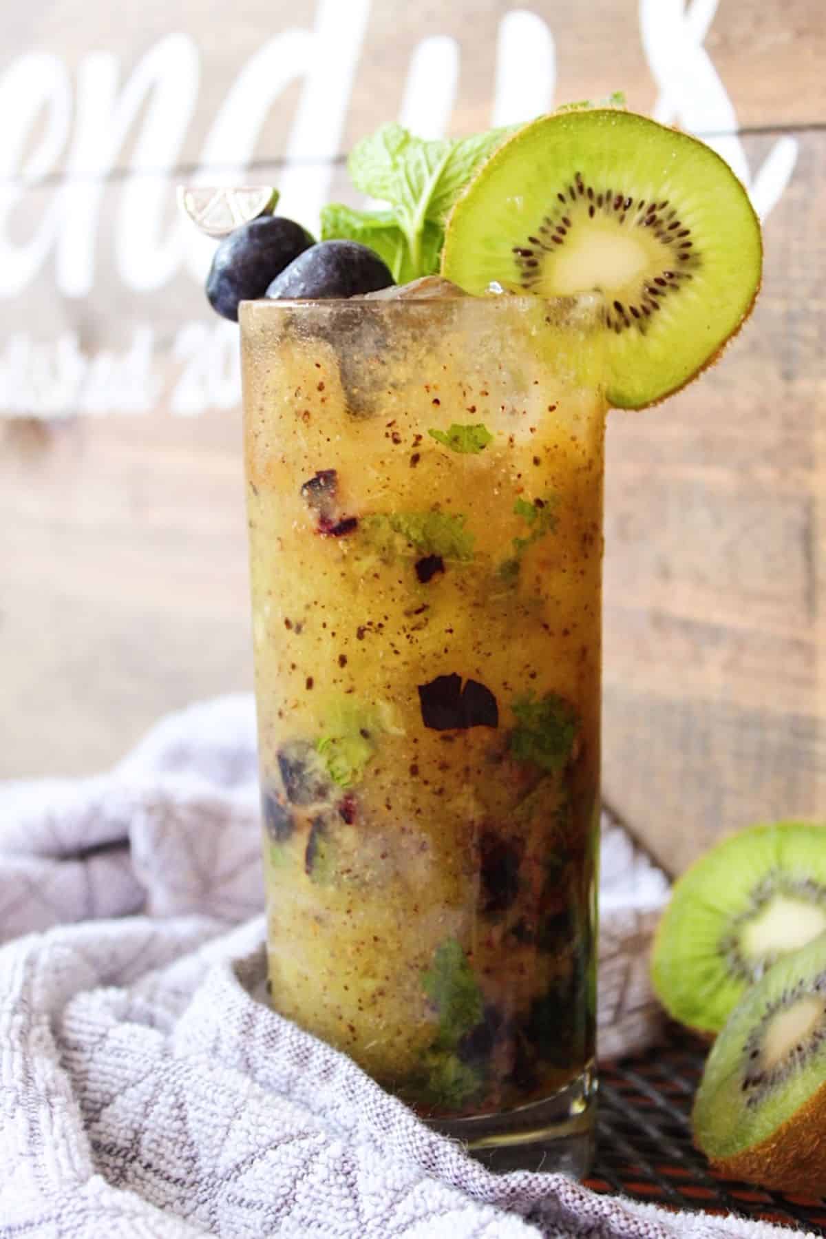 Kiwi blueberry mojito garnished with kiwi slice next to grey towel.