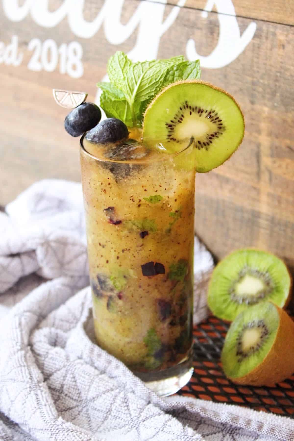 Blueberry mojito in a glass in front of wood backdrop.