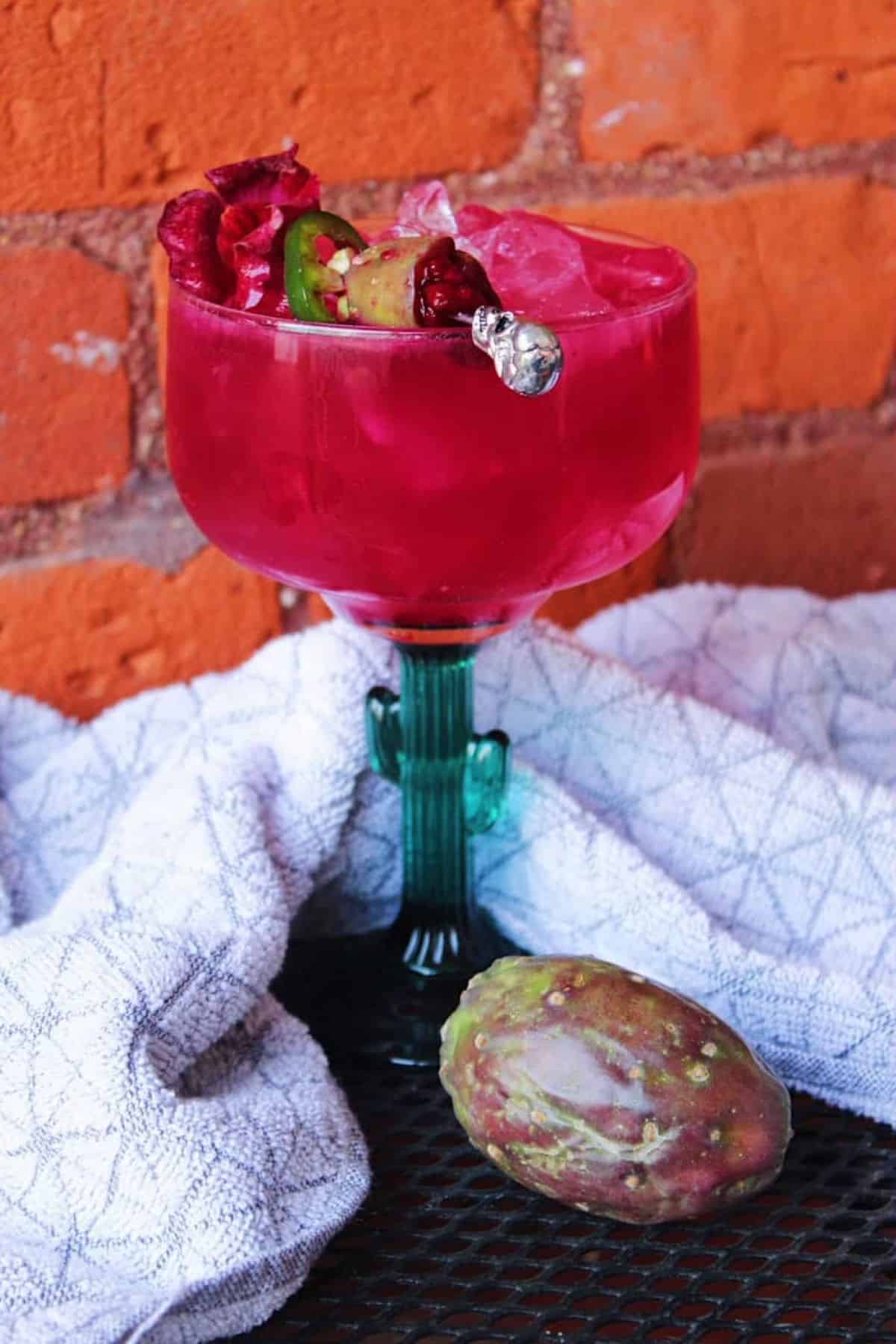 Cactus glass containing pink prickly pear margarita against brick wall.
