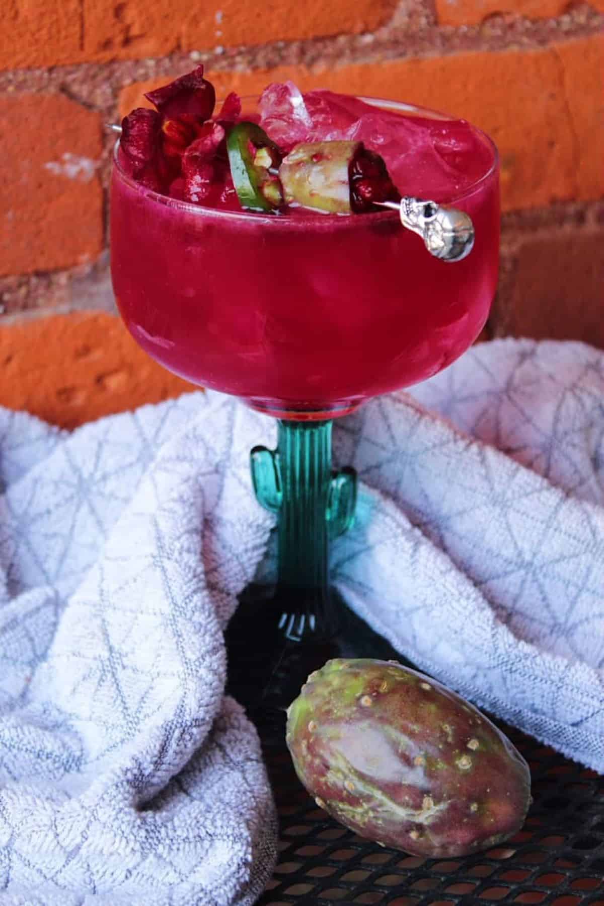 Electric pink prickly pear margarita on the rocks in a cactus shaped glass.