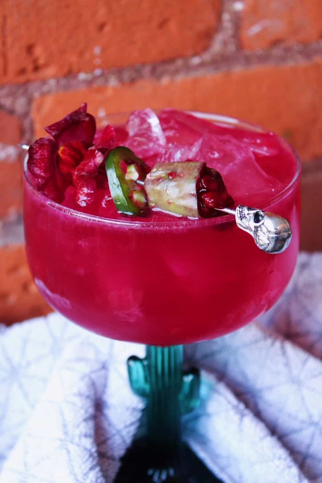 Close shot of vibrant pink prickly pear margarita garnished with slice of jalapeno.