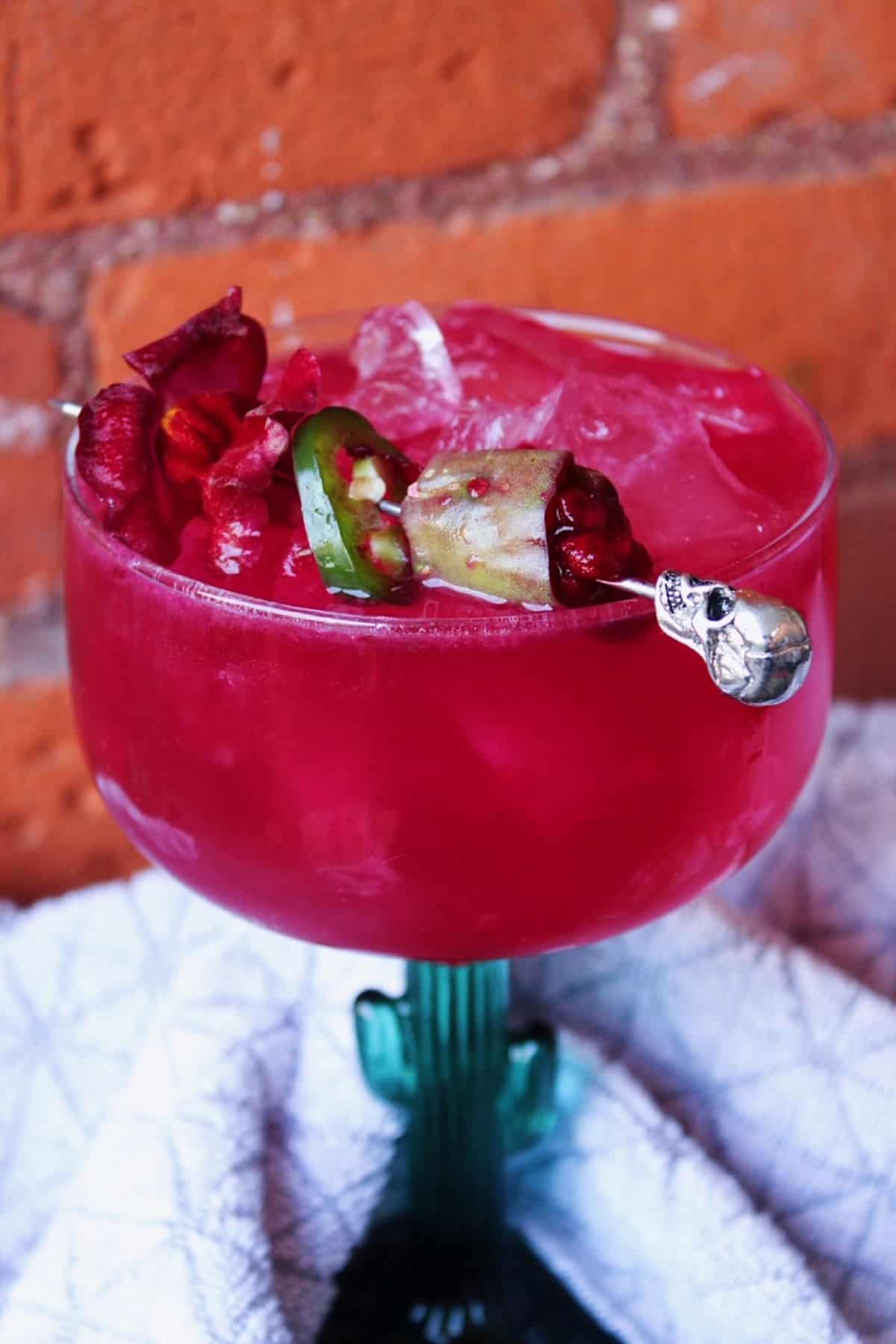 Close shot of vibrant pink prickly pear margarita garnished with slice of jalapeno. 