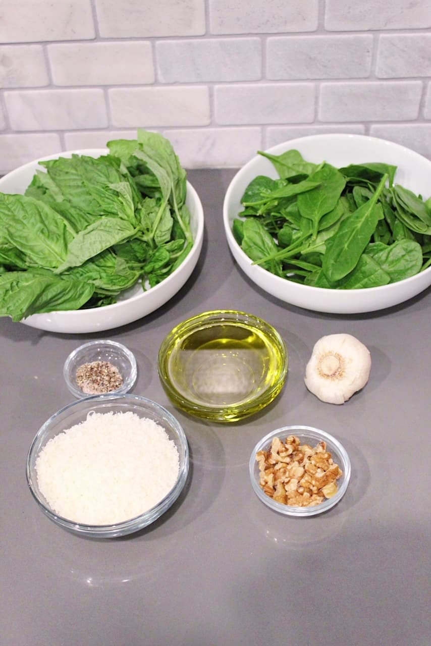 Bowls of fresh basil, spinach, fresh Parmesan, walnuts, olive oil, salt, pepper and garlic to make pesto.