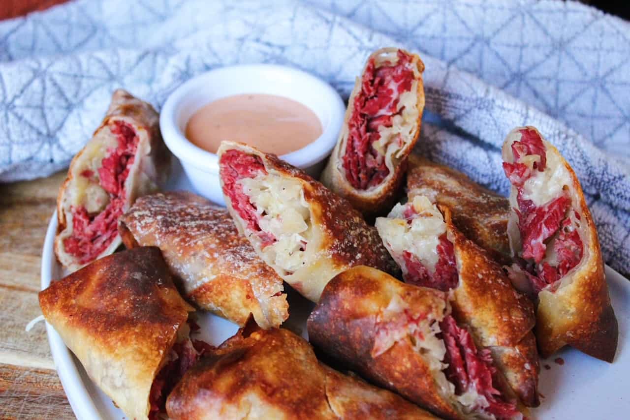 Reuben egg rolls close up on white serving plate with grey dish towel.