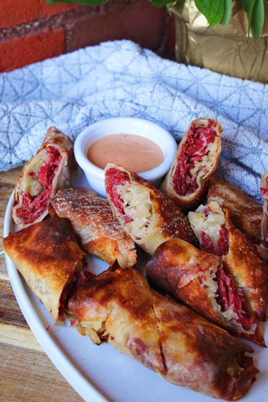 Reuben Egg Rolls on white serving plate with dipping sauce.